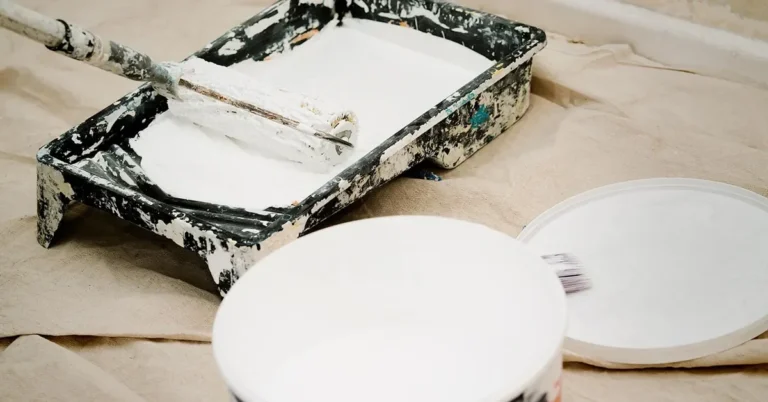 Paint roller in a tray next to an open paint bucket on a drop cloth