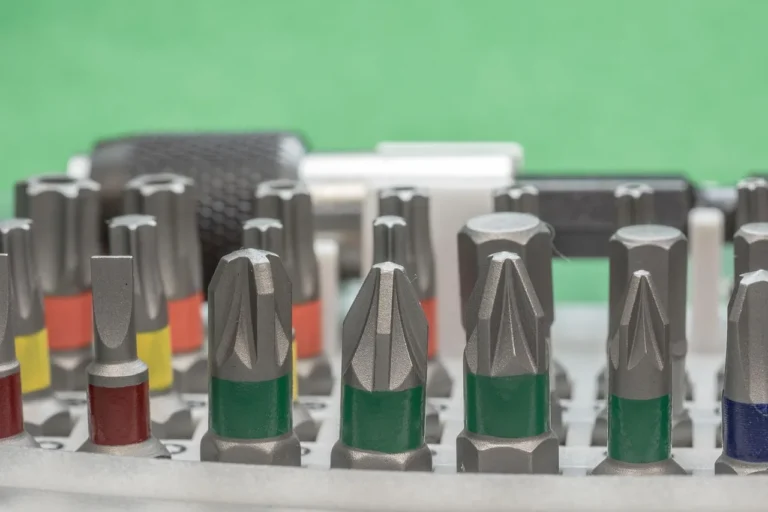 Impact driver bits and assorted screws arranged beside a cordless impact driver on a workbench